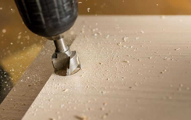 Bohrer arbeitet sich in ein Holzbrett, Holzspäne fliegen