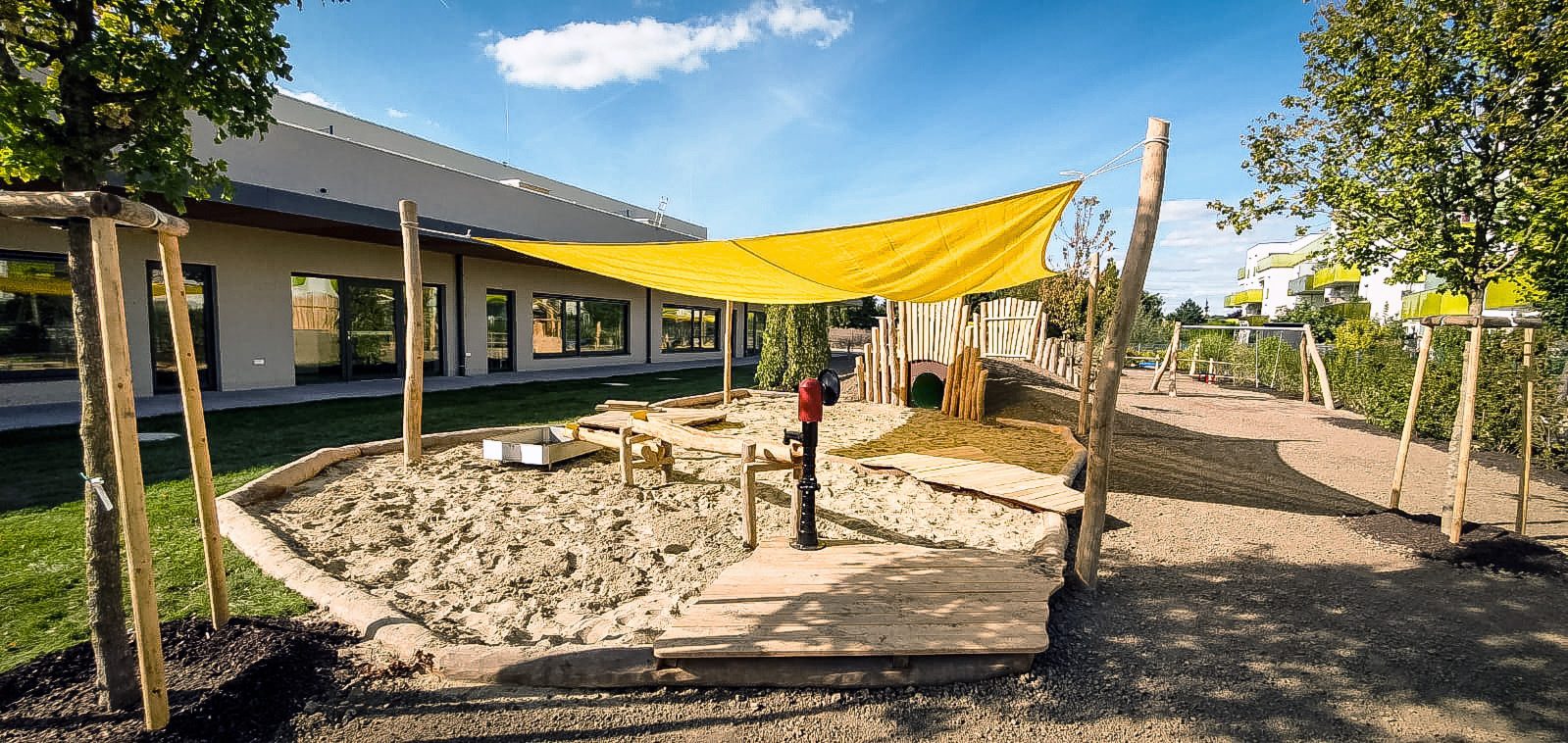 Sandspielbereich mit Sonnensegel vor einem Kindergarten