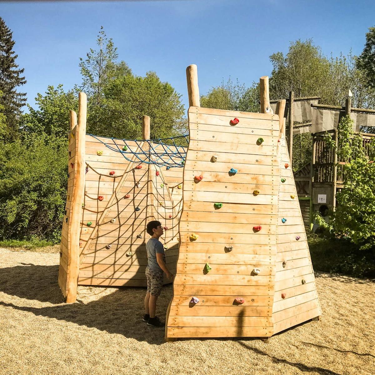 Kletterwand aus Holz mit farbigen Griffen und Kletternetz