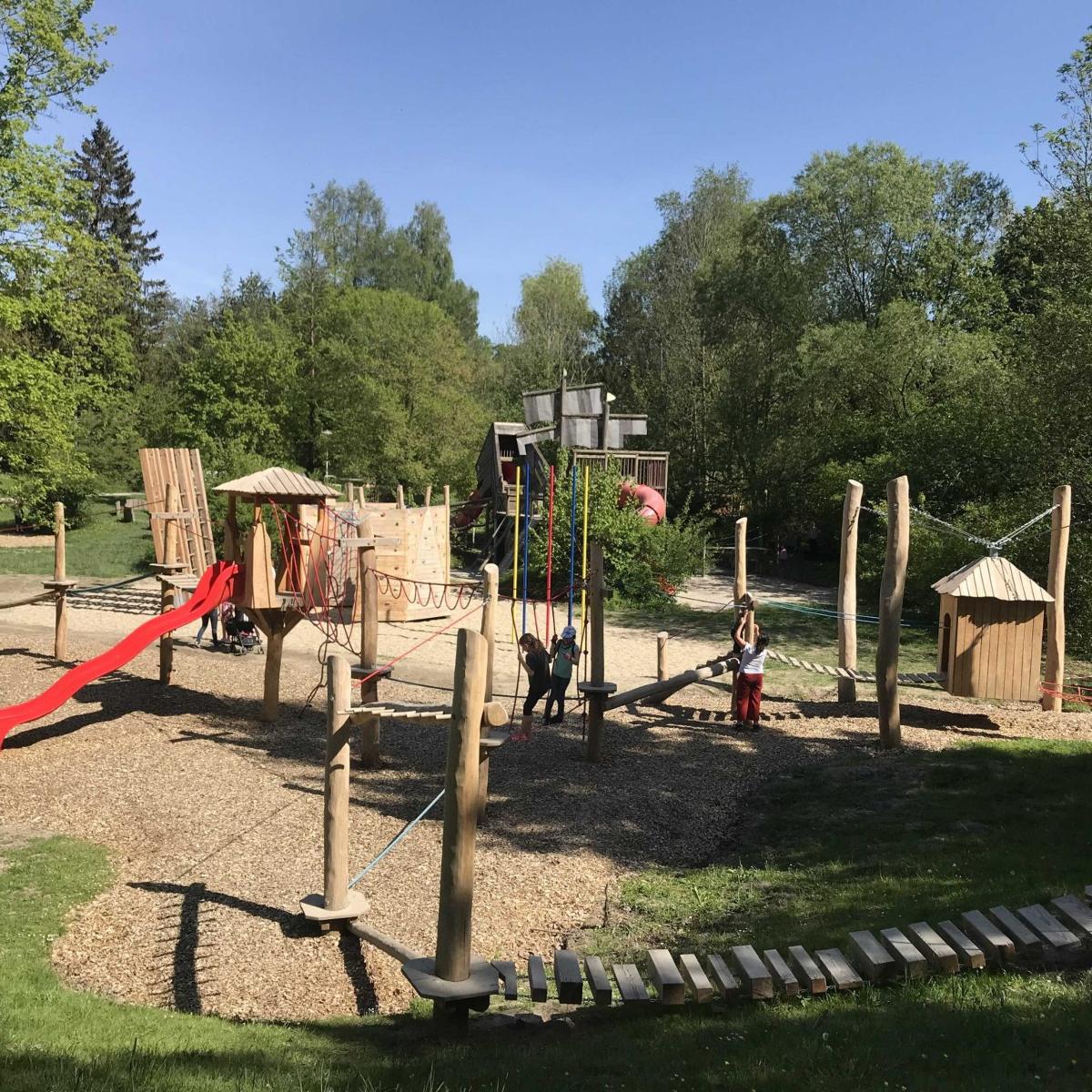 Blick über eine Parkanlage mit Kletterturm, Rutsche und Balancierweg