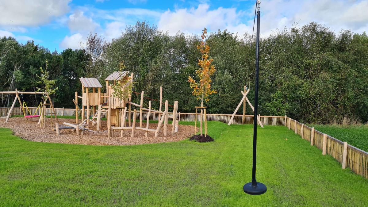 Neu errichteter Spielplatz aus Holz mit Spieltürmen und Holzzaun auf einer Wiese