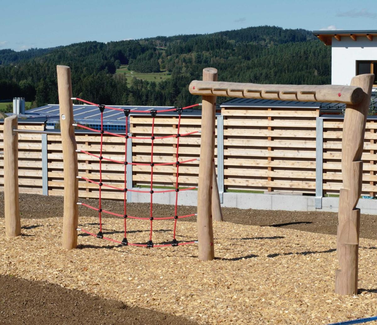 Kletternetz und Reckstange aus Holz auf einem Spielplatz mit Rindenmulch
